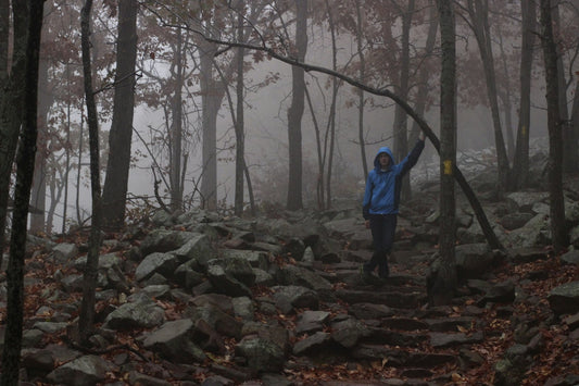 Hombre con chaqueta de montaña de pie sobre una roca en medio del bosque observando el entorno