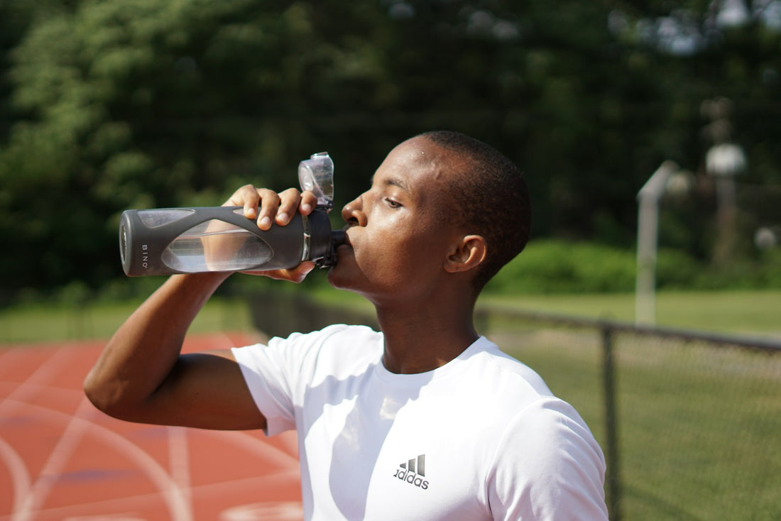 Persona bebiendo agua de una botella deportiva durante una actividad al aire libre