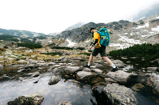 Senderista con mochila cruzando una corriente de agua en la montaña